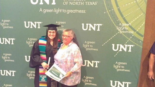 Graduate and family member posing in front of a UNT banner